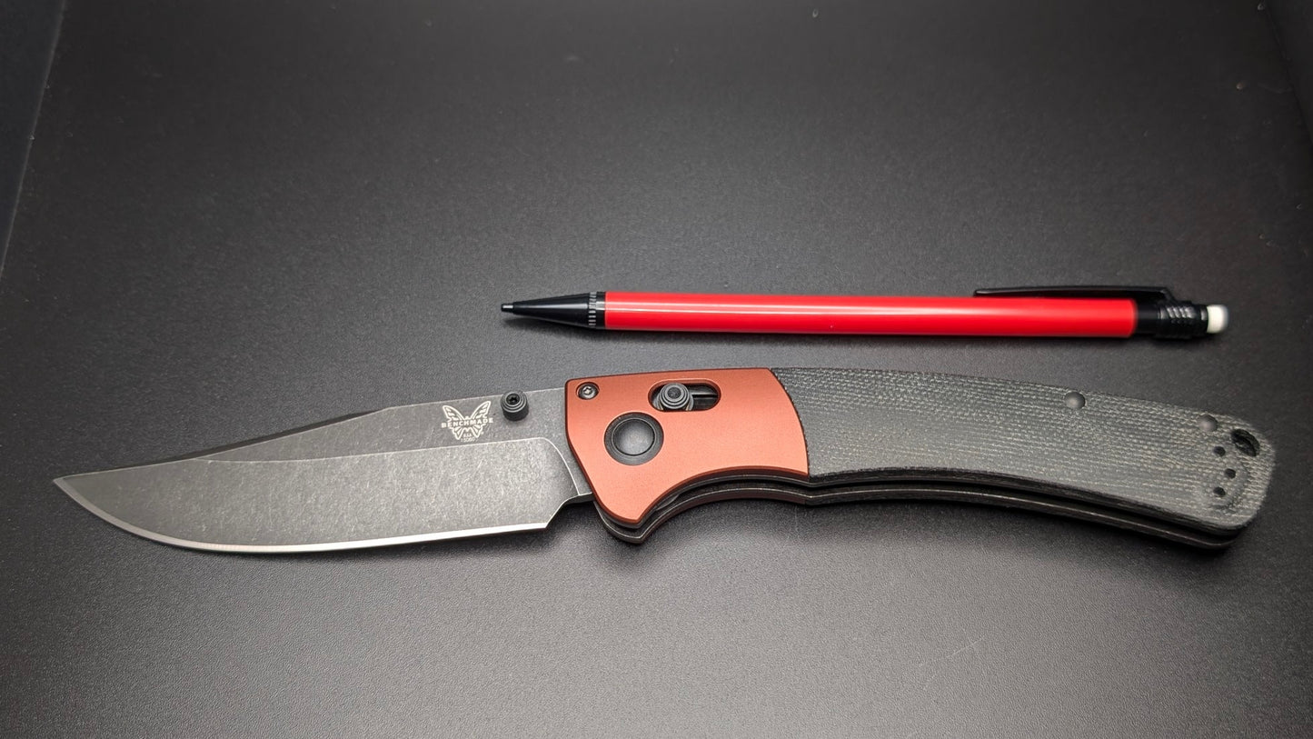 Folding knife with a red pencil and black handle on a dark surface