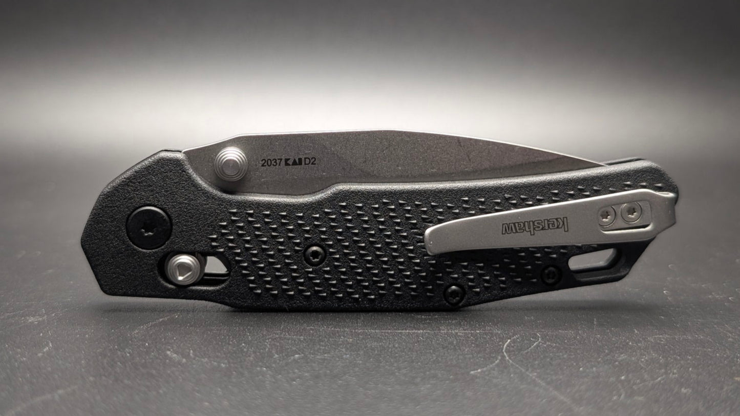 Black folding knife on a gray surface with a dark background