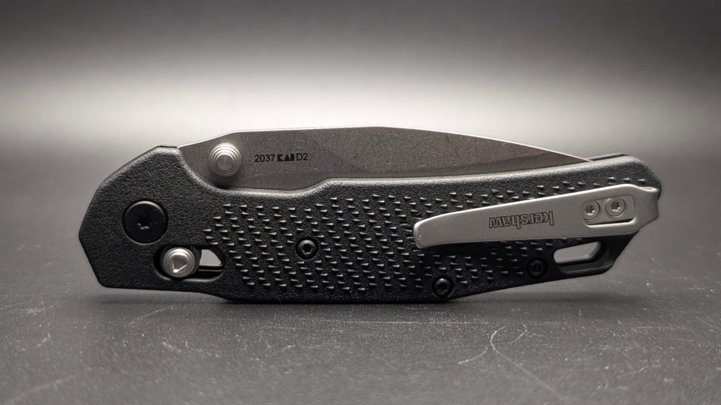 Black folding knife on a gray surface with a dark background