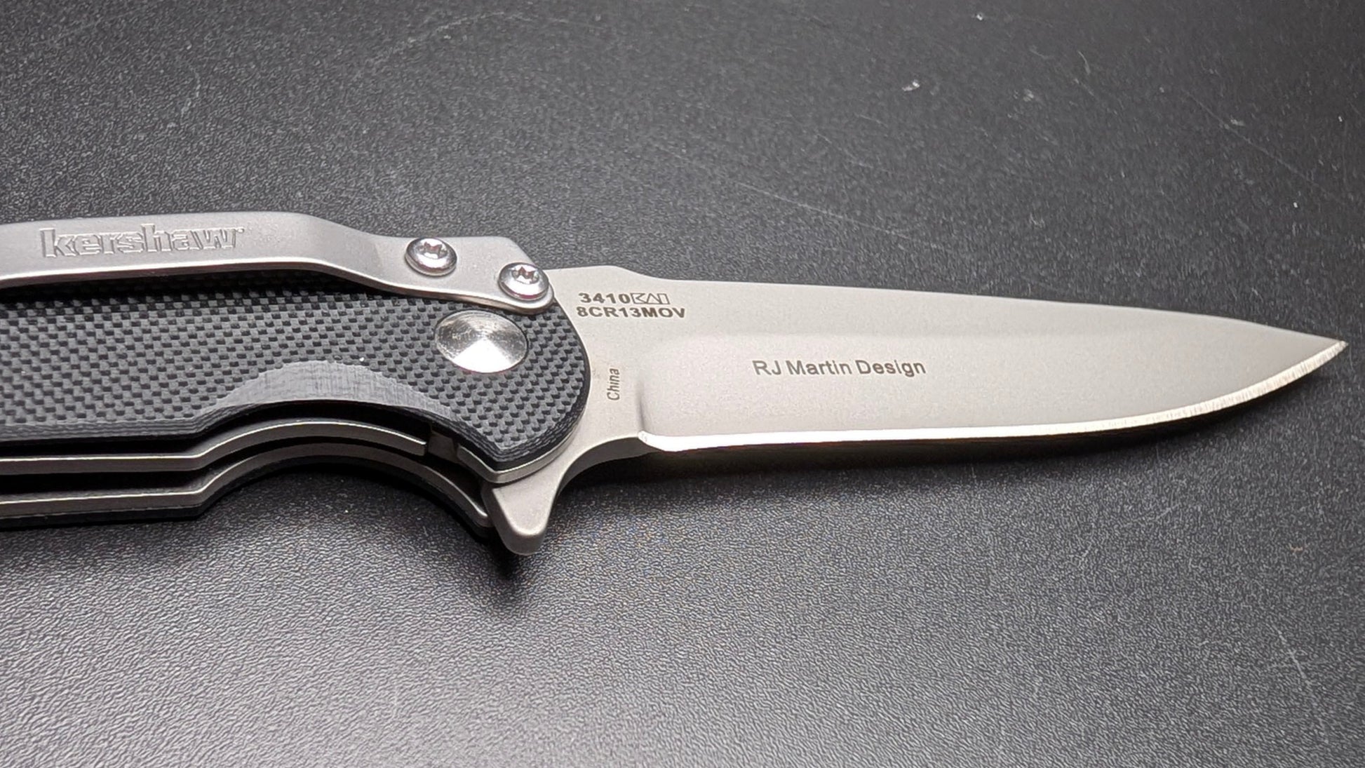 Folding knife with a metallic blade and black handle on a dark surface
