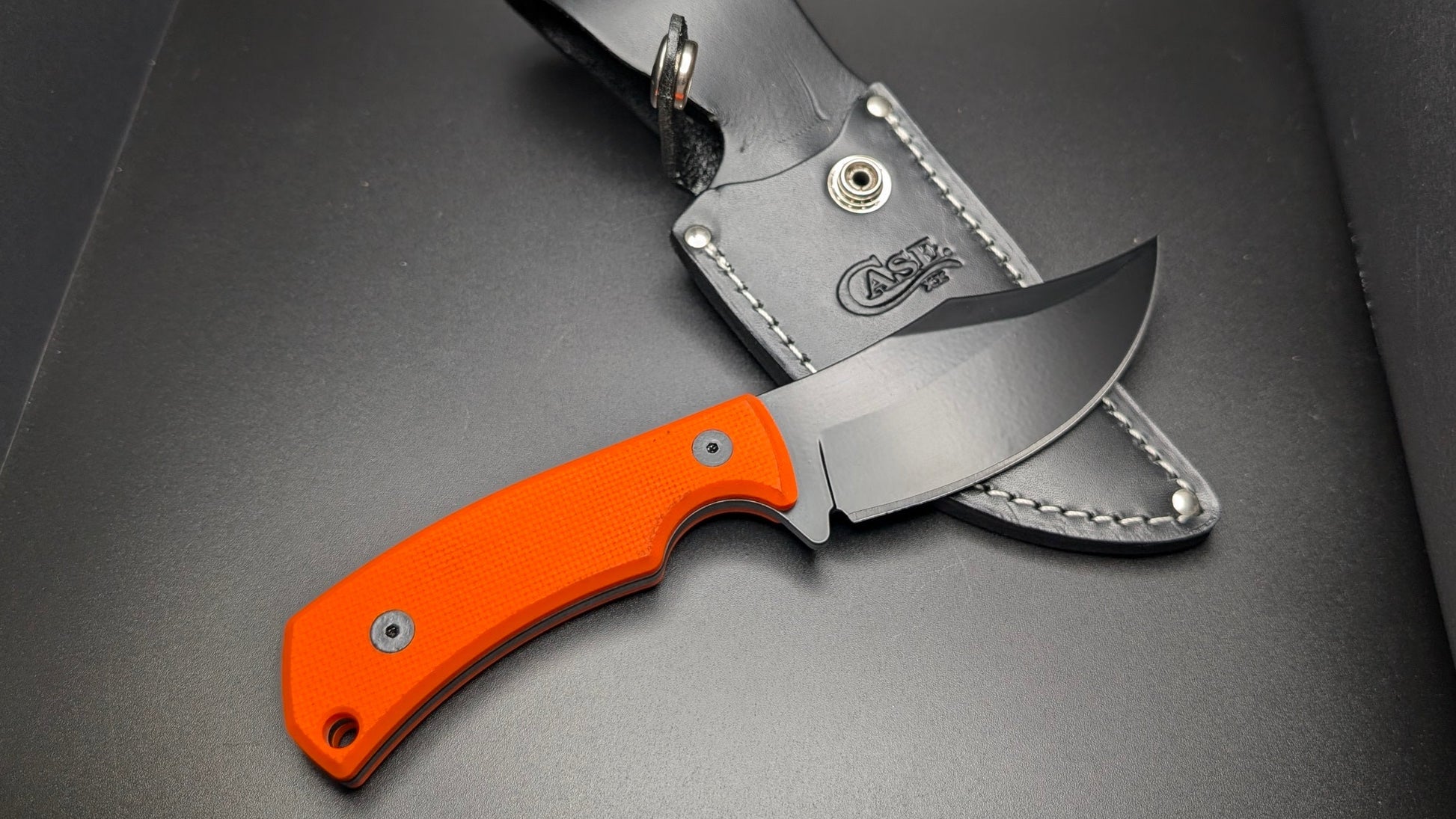 Knife with orange handle and leather sheath on a gray background