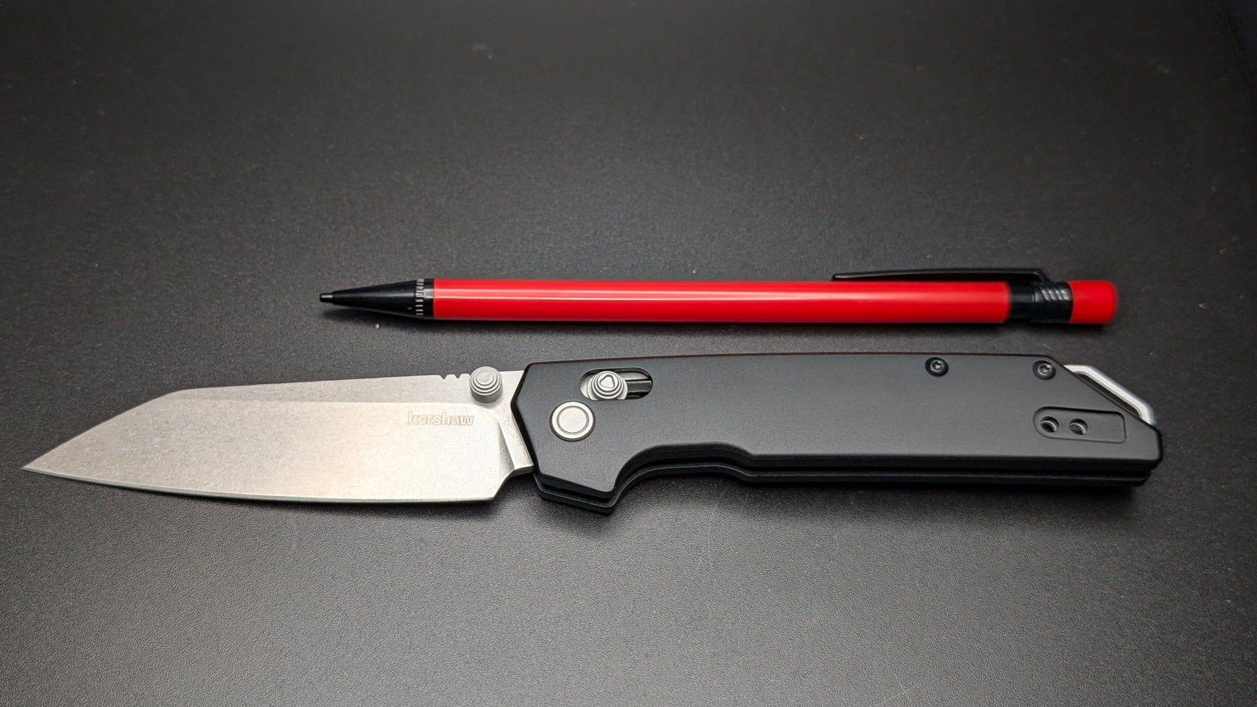 Folding knife and pen on a dark surface