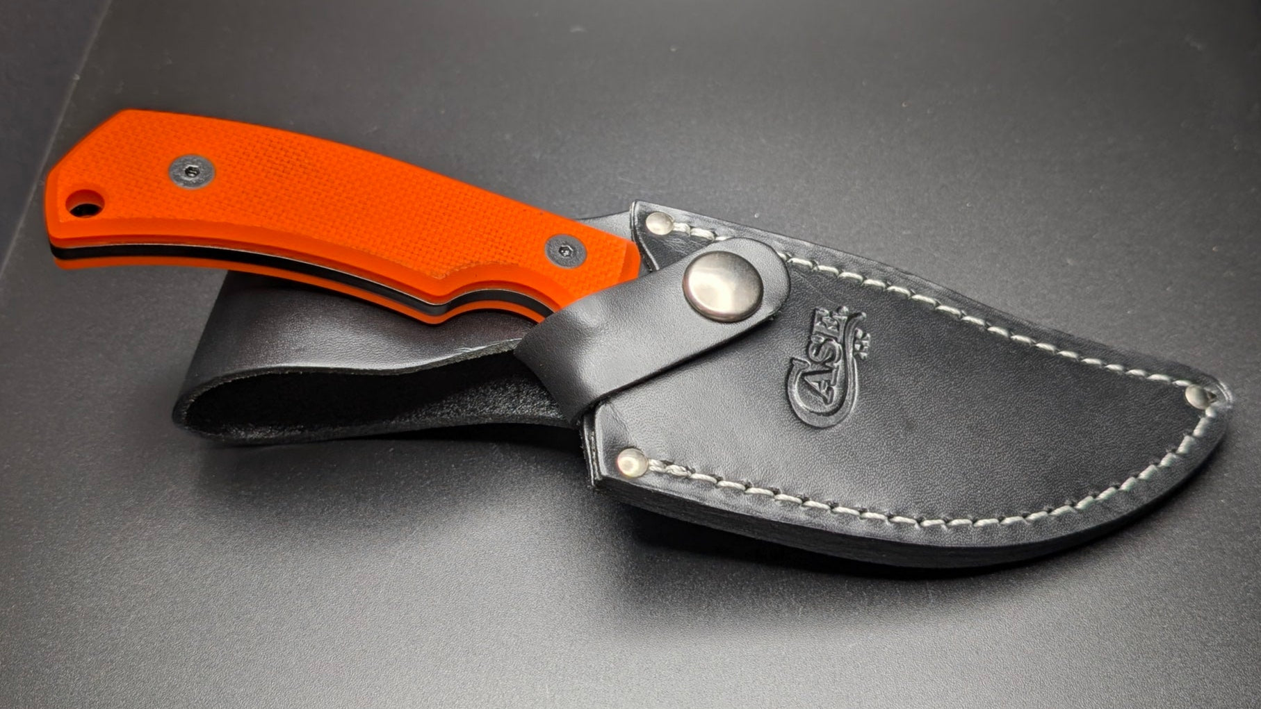 Folding knife with orange handle and black sheath on a gray surface