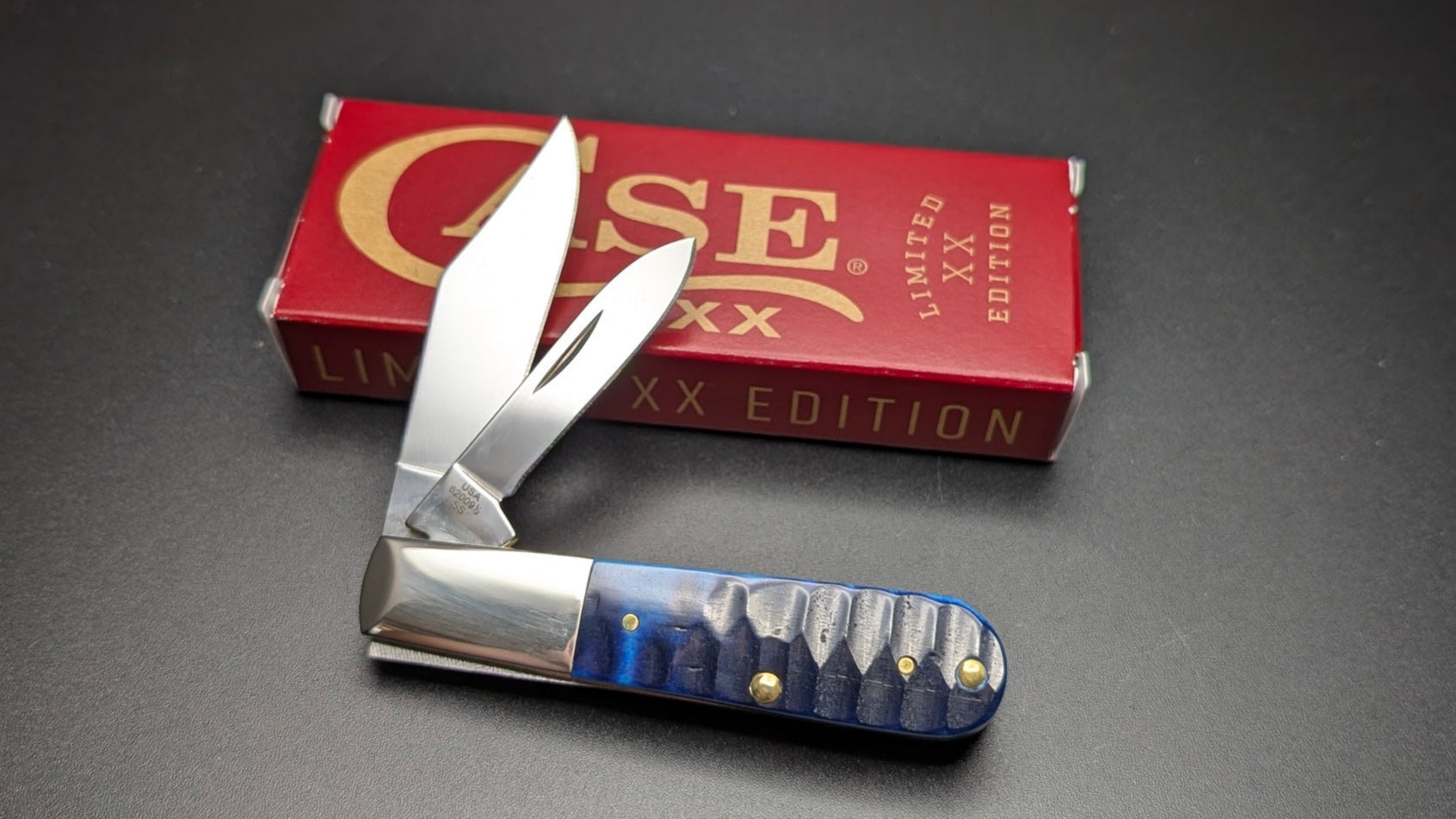 Small pocket knife with blue handle and silver blade next to a red 'Case' box on a dark surface