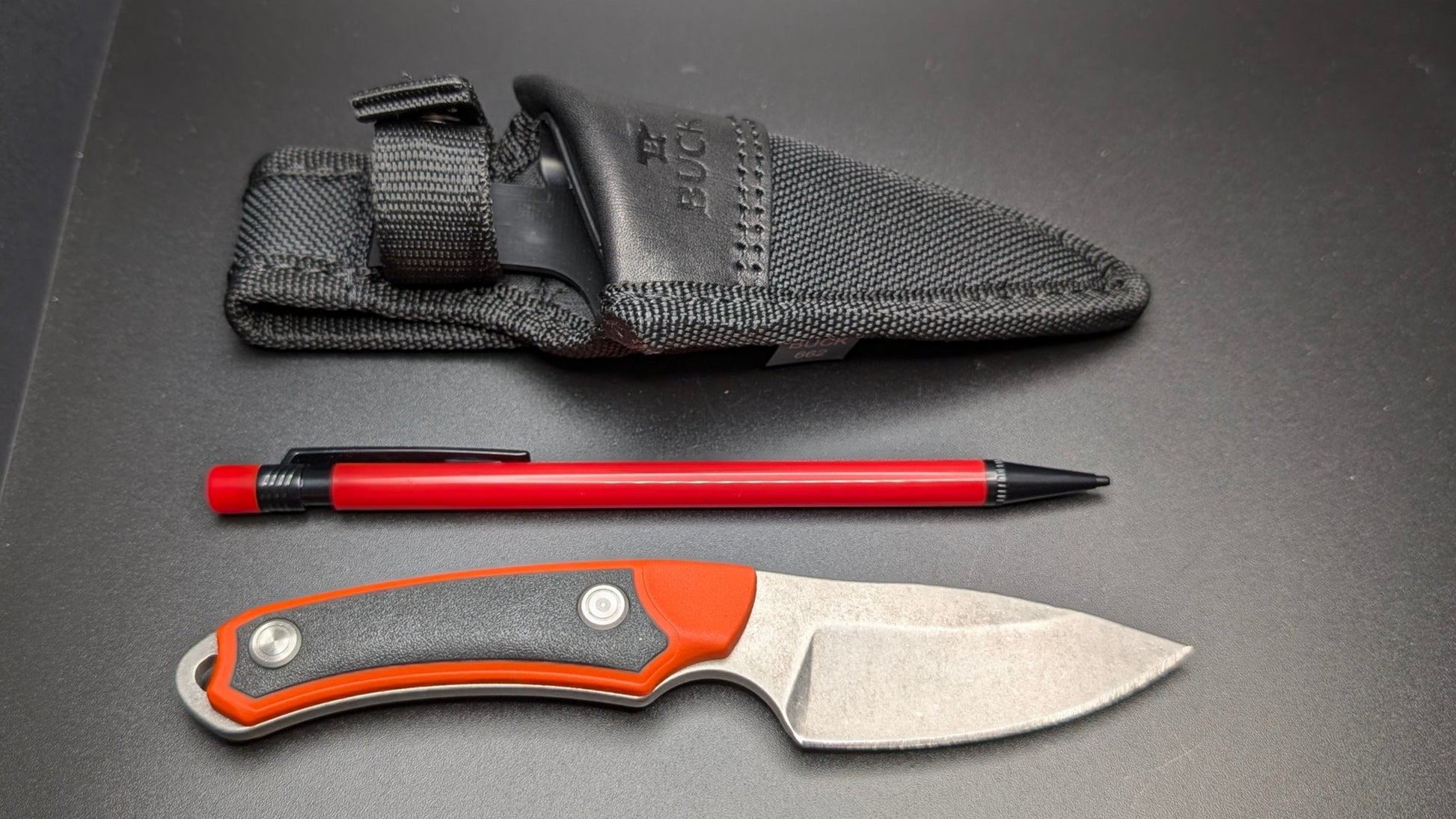Fixed blade and black Sheath, pen, and sheath on a gray surface