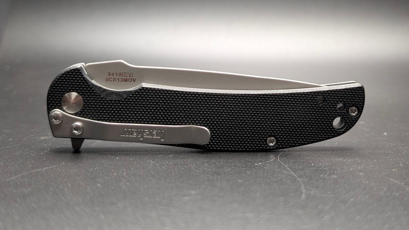 Black folding knife on a gray surface with a dark background