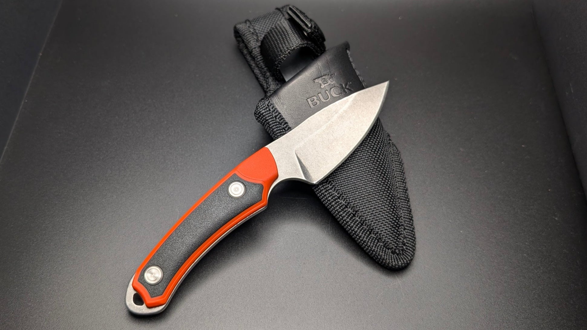 Knife with orange handle and black sheath on a dark surface
